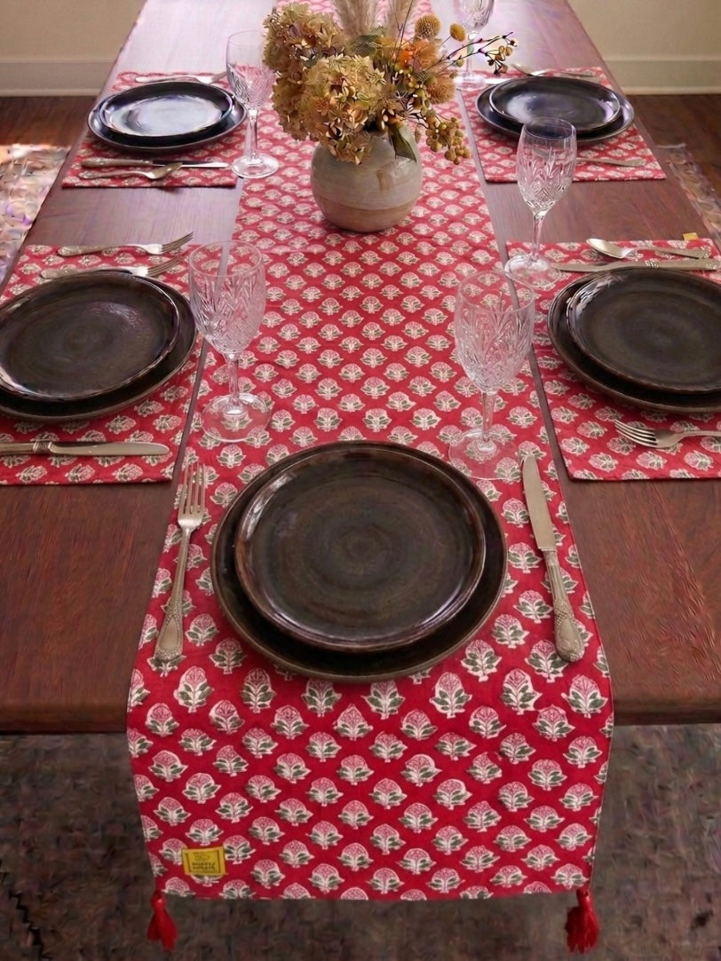 House of Mulmul - Blockprinted Cotton Reversible Table Runner & Mats set. Dining table set with a red patterned table runner, black plates, and silverware.