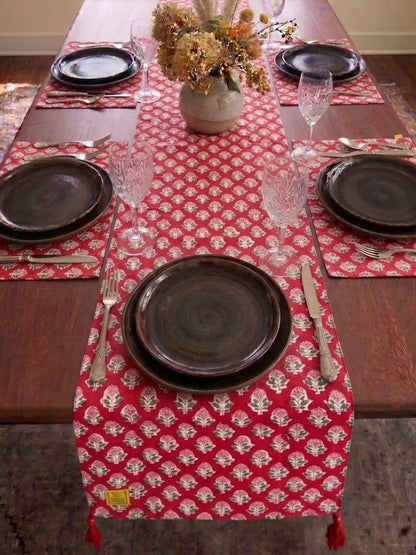 House of Mulmul - Blockprinted Cotton Reversible Table Runner & Mats set. Dining table set with a red patterned table runner, black plates, and silverware.