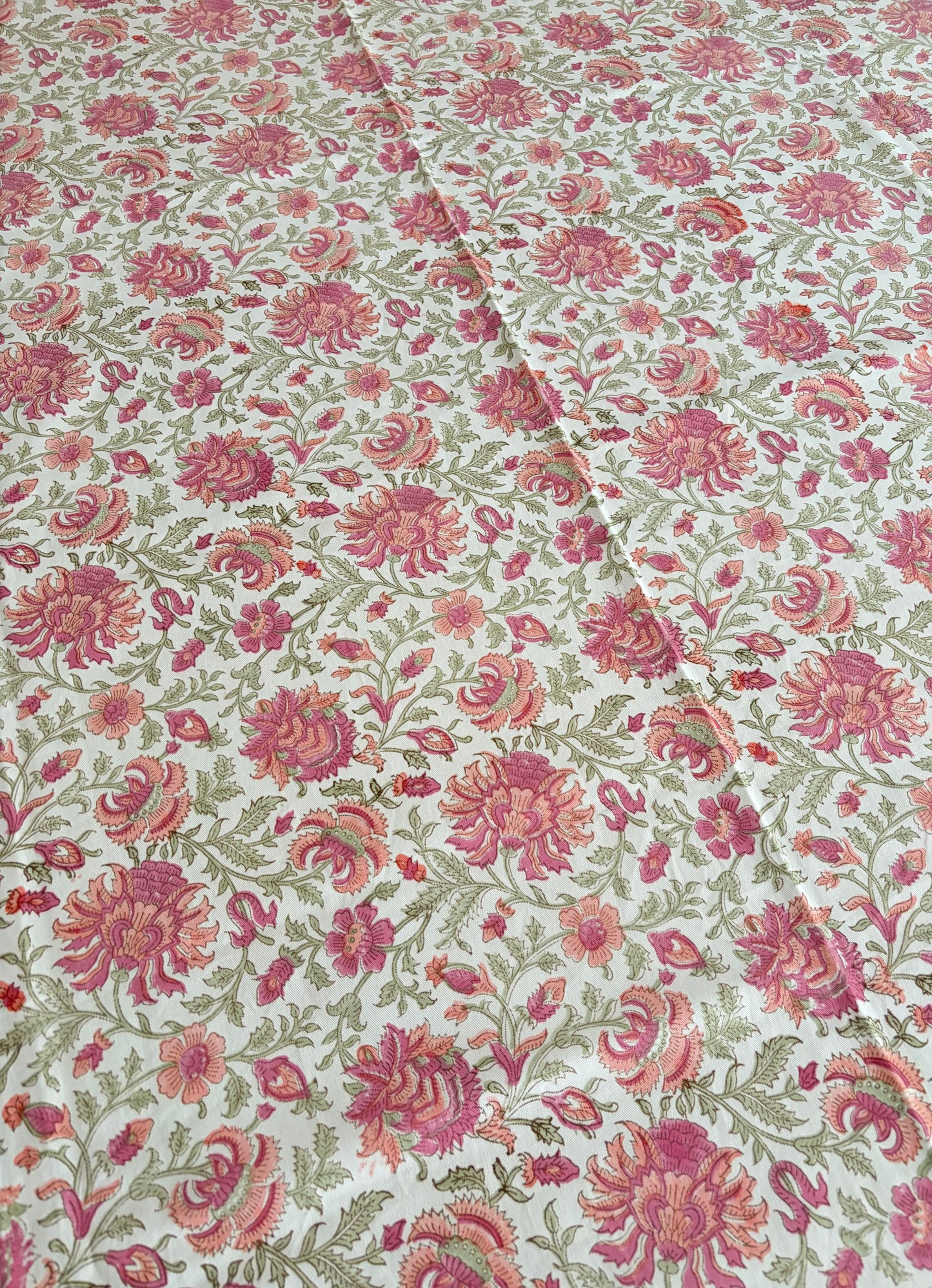 House of Mulmul - Blockprinted Cotton Table Cloth. A close-up of a floral fabric with a repeating pattern of pink and red flowers with green leaves on a cream background.