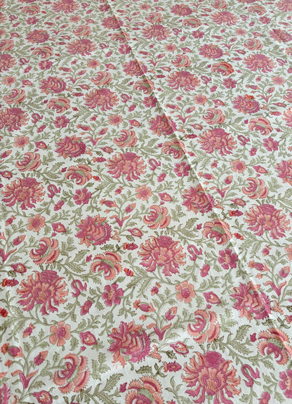 House of Mulmul - Blockprinted Cotton Table Cloth. A close-up of a floral fabric with a repeating pattern of pink and red flowers with green leaves on a cream background.