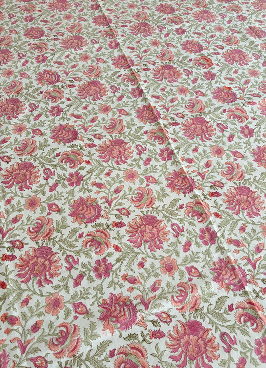House of Mulmul - Blockprinted Cotton Table Cloth. A close-up of a floral fabric with a repeating pattern of pink and red flowers with green leaves on a cream background.