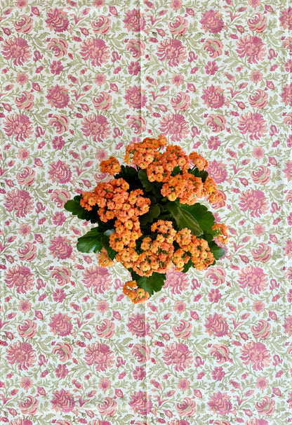 House of Mulmul - Blockprinted Cotton Table Cloth. A cluster of orange flowers with green leaves arranged in the center of a pink and green floral patterned background.