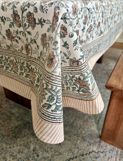 House of Mulmul - Blockprinted Cotton Table Cloth. A cream-colored tablecloth with a detailed botanical block print in sage green and terracotta orange, draped over a table in a home setting.