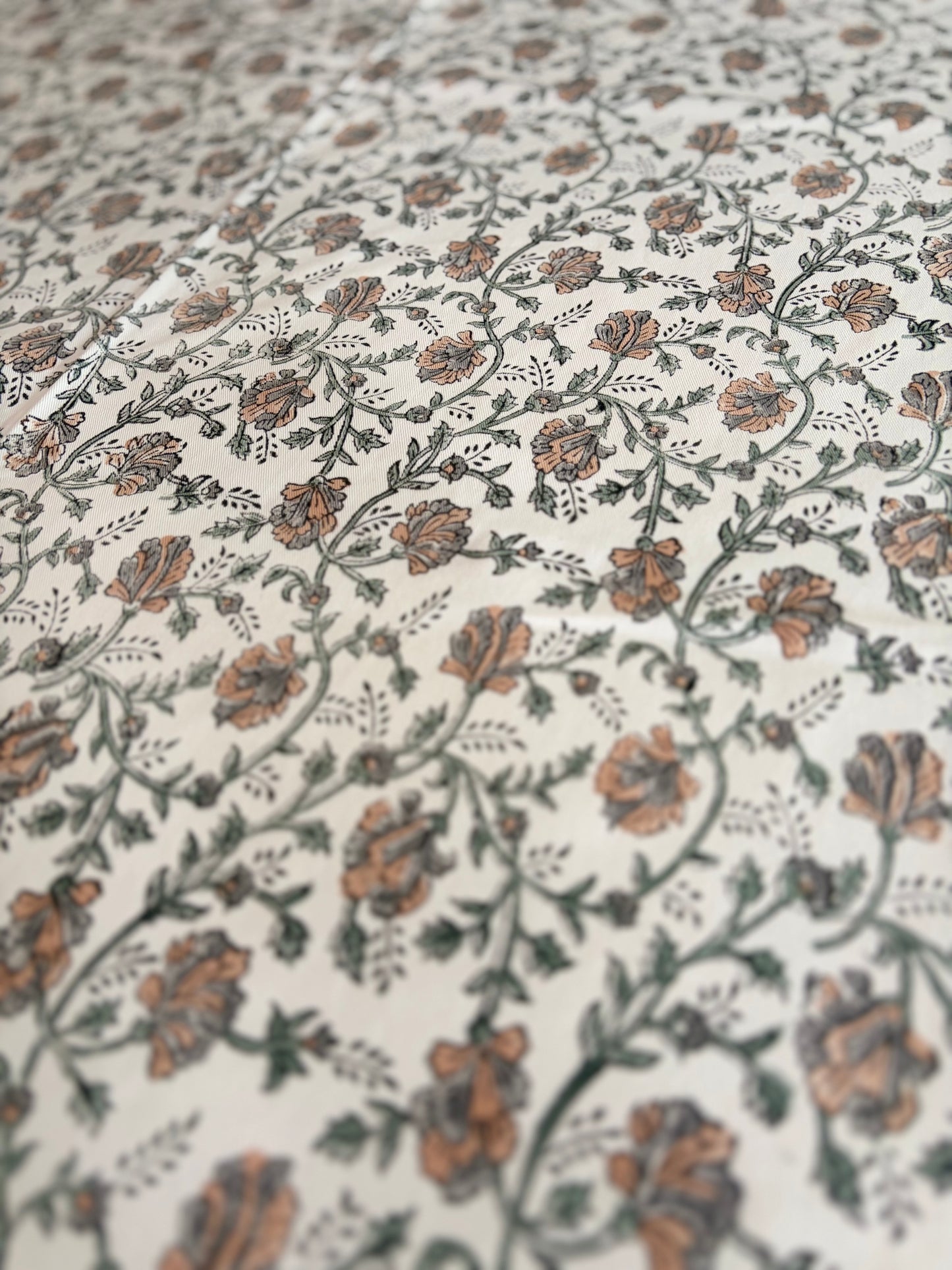 House of Mulmul - Blockprinted Cotton Table Cloth. A close-up of a fabric or wallpaper pattern featuring delicate floral vines in muted terracotta orange, olive green, and gray on an off-white background.