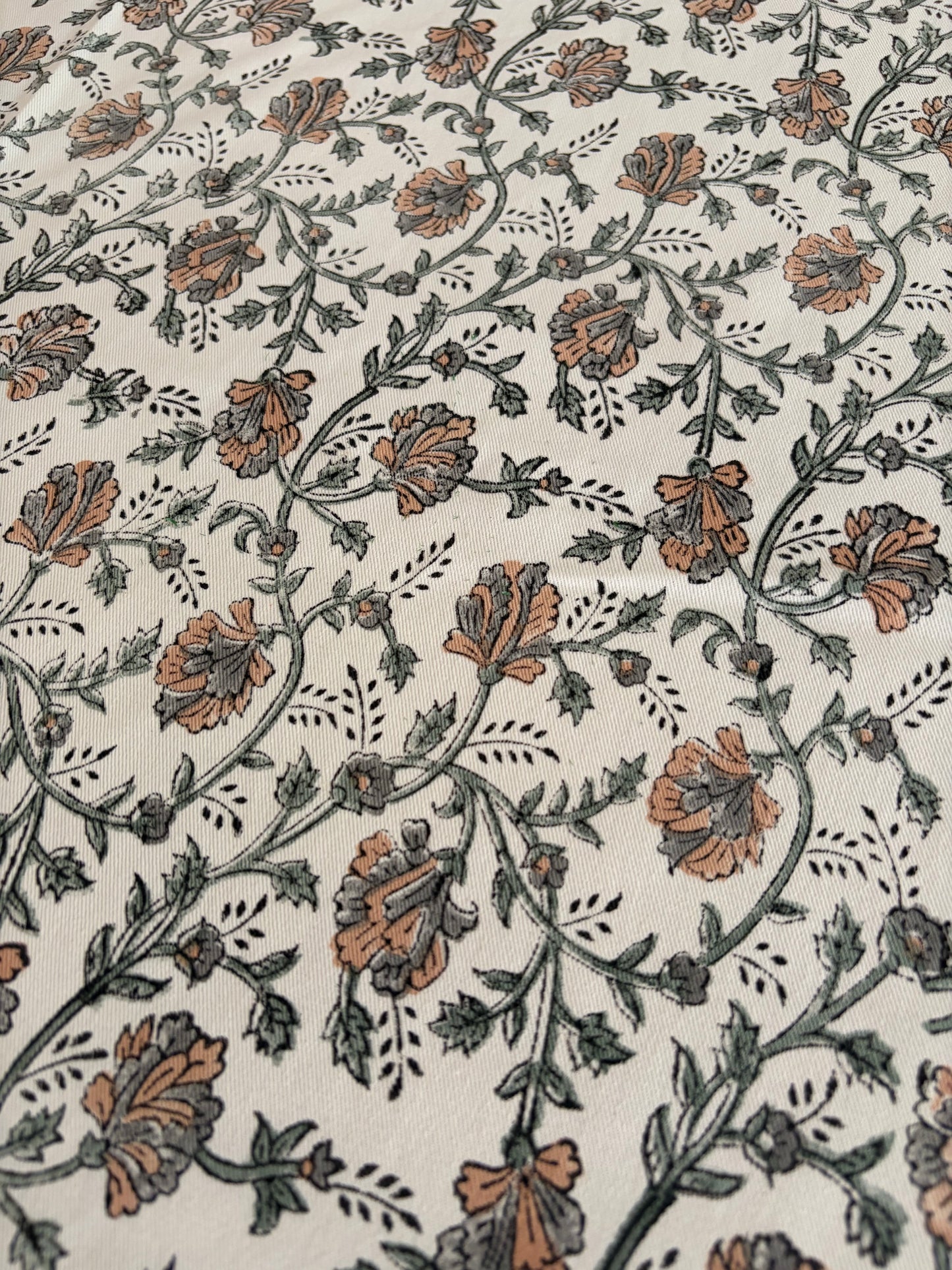 House of Mulmul - Blockprinted Cotton Table Cloth. A close-up of a fabric or wallpaper pattern featuring a repeating floral vine design in muted brown and gray on an off-white background.
