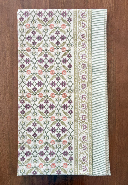 House of Mulmul - Blockprinted Cotton Table Cloth. A rectangular cotton table runner with an intricate block-printed floral pattern, laid flat on a dark brown wooden surface. The runner features a central panel with purple and pink flowers on a green and white geometric lattice, flanked by two borders with striped and floral details.