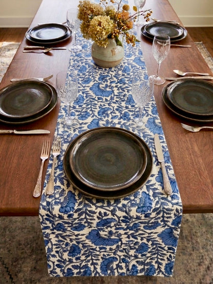 House of Mulmul - Blockprinted Cotton Reversible Table Runner & Placemats set. Dining table set with blue and white patterned table runner, dark plates, and silverware.