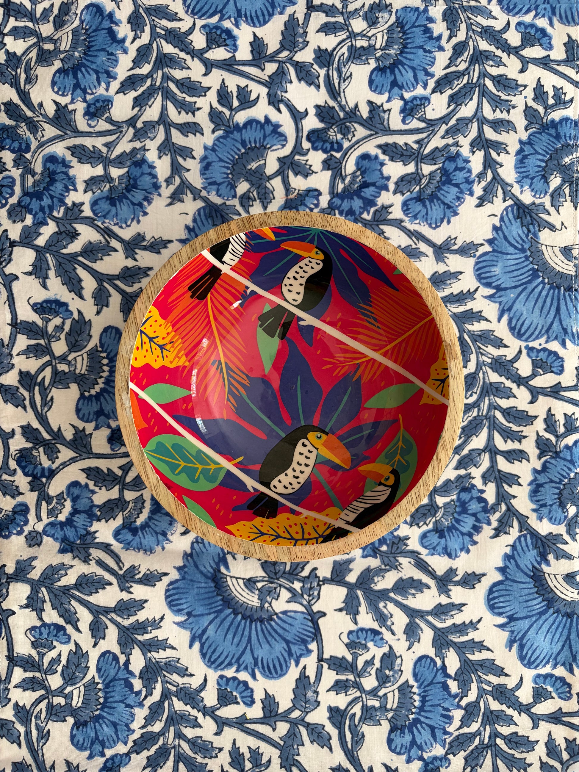House of Mulmul - Blockprinted Cotton Reversible Table Runner & Placemats set. Decorative plate with a colorful bird design on a blue floral patterned fabric background