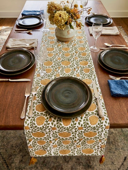 House of Mulmul - Blockprinted Cotton Reversible Table Runner & Placemats set. Dining table set with patterned table runner, dark plates, and floral centerpiece.