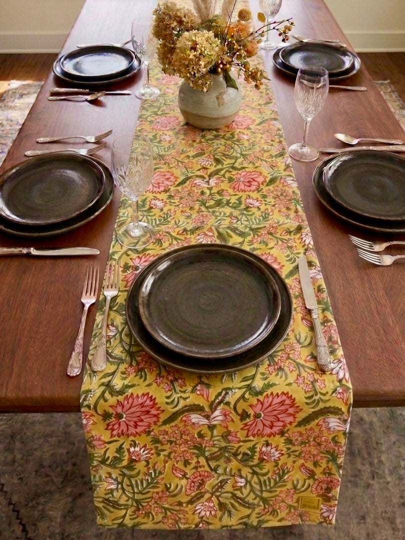 House of Mulmul - Blockprinted Cotton Reversible Table Runner & Placemats set. Set dining table with floral table runner, plates, and cutlery.