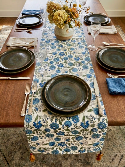House of Mulmul - Blockprinted Cotton Reversible Table Runner & Placemats set. Dining table set with floral table runner, plates, and cutlery on a wooden floor.