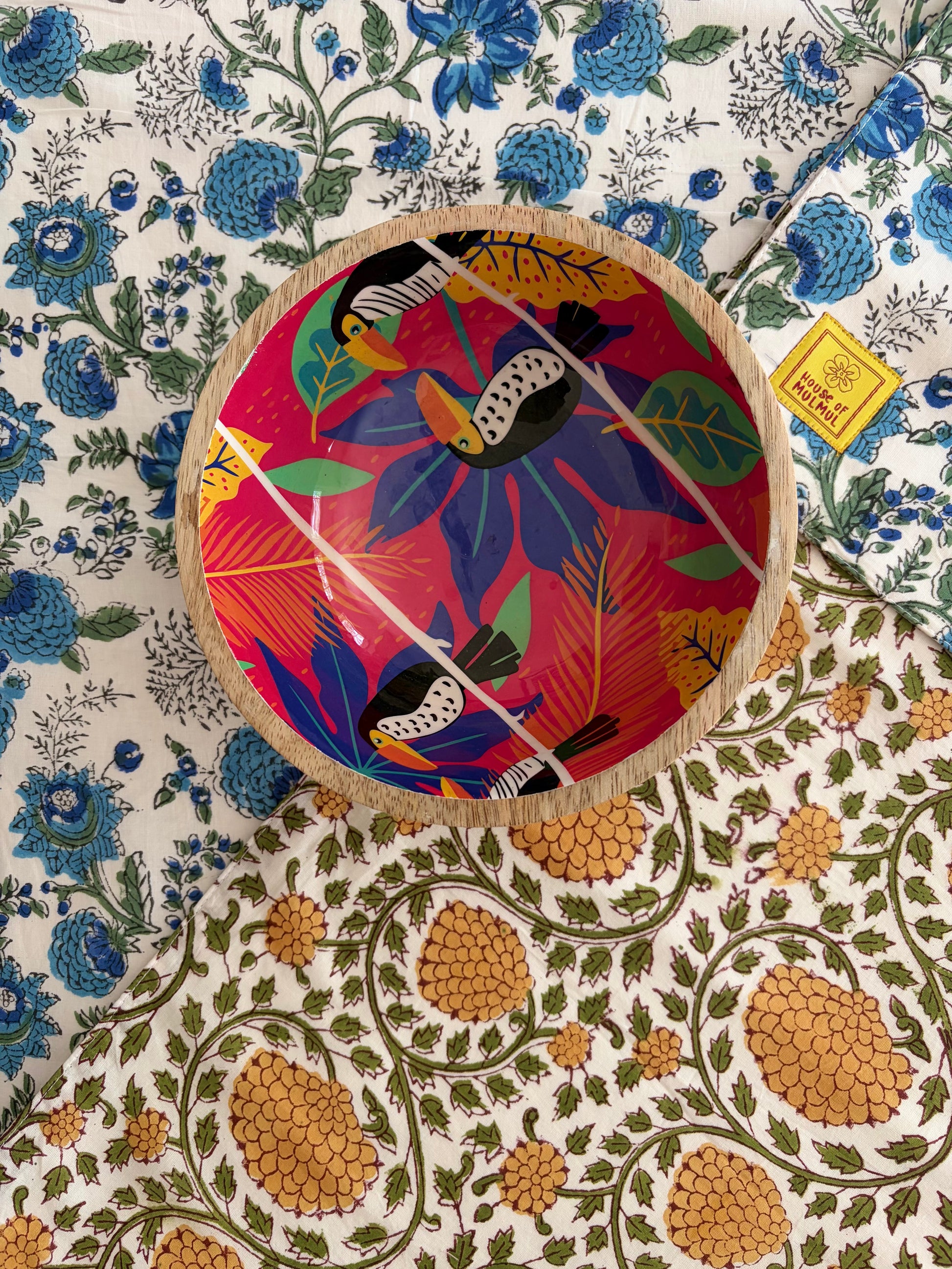 House of Mulmul - Blockprinted Cotton Reversible Table Runner & Placemats set. Decorative plate with colorful bird design on a floral patterned surface
