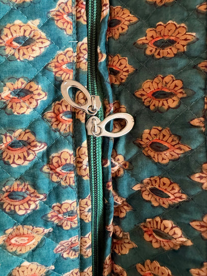 House of Mulmul - Blockprinted Cotton Tote Bags. Close-up of a quilted fabric with a teal and orange floral pattern, featuring a green zipper and a silver metal zipper pull.