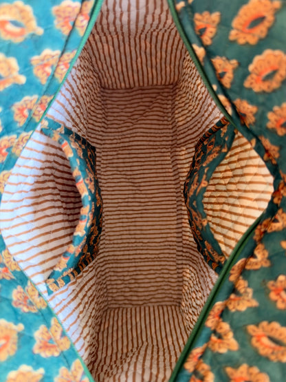 House of Mulmul - Blockprinted Cotton Tote Bags. Close-up of a quilted fabric bag's interior, showing a striped beige and brown lining with teal and orange floral patterned fabric lining the sides.