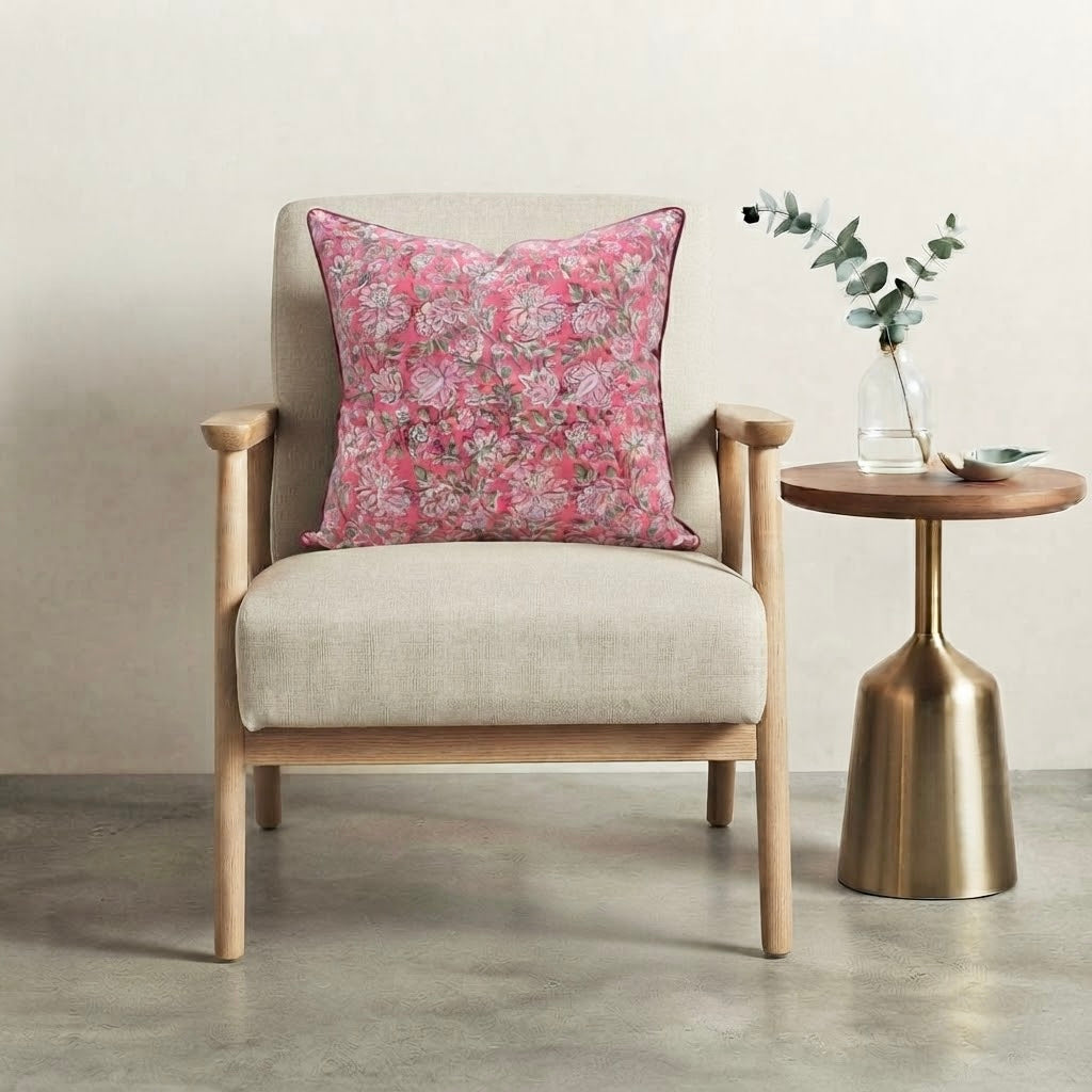 House of Mulmul - Blockprinted Cushion Covers-Pillow Cases. A light beige upholstered armchair with a pink floral throw pillow, shown next to a round wooden side table with a gold metal pedestal base in a minimalist room setting.