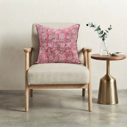 House of Mulmul - Blockprinted Cushion Covers-Pillow Cases. A light beige upholstered armchair with a pink floral throw pillow, shown next to a round wooden side table with a gold metal pedestal base in a minimalist room setting.
