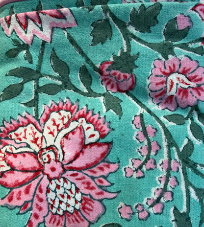 House of Mulmul - Blockprinted Cushion Covers-Pillow Cases. A close-up of a printed textile or fabric pattern featuring large pink and white flowers, smaller pink buds, and dark green leaves on a turquoise background.