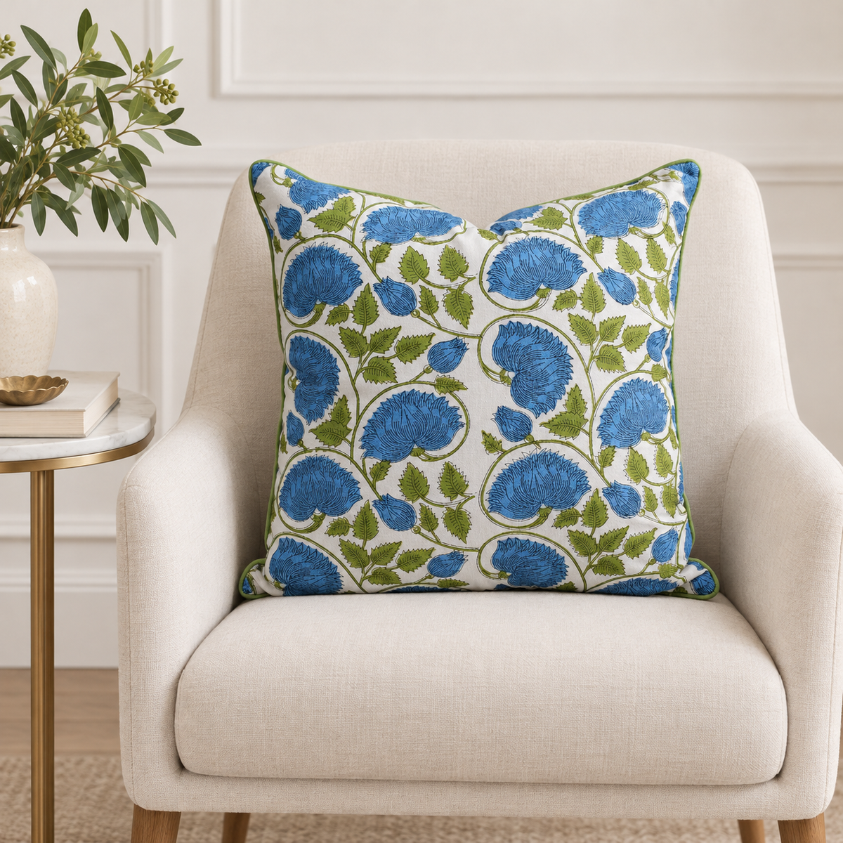 House of Mulmul - Blockprinted Cushion Covers-Pillow Cases. A square throw pillow with a blue and green floral pattern on a white background, styled on a light beige armchair next to a side table with a plant.
