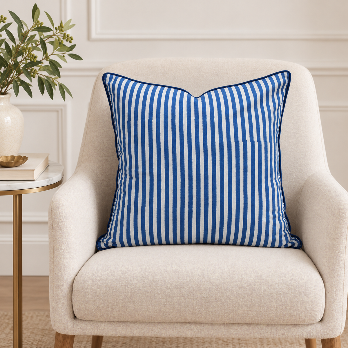 House of Mulmul - Blockprinted Cushion Covers-Pillow Cases. A square throw pillow with vertical blue and white stripes sits on a cream upholstered armchair in a styled interior setting with a side table and plant.