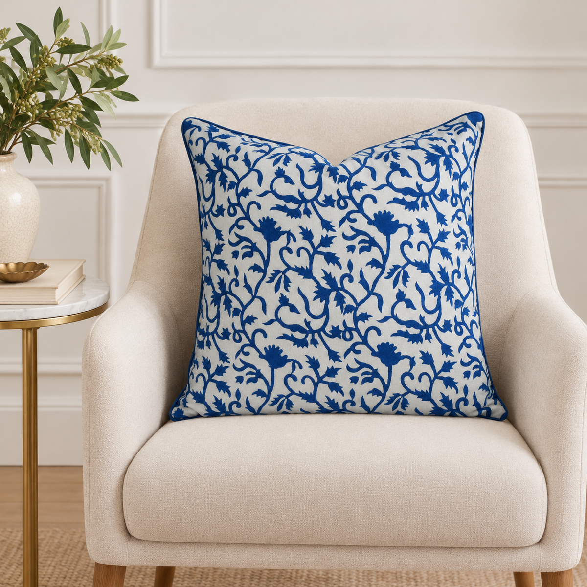 House of Mulmul - Blockprinted Cushion Covers-Pillow Cases. A square throw pillow with a blue floral damask pattern on a white background, styled on a cream-colored armchair next to a side table with a plant.