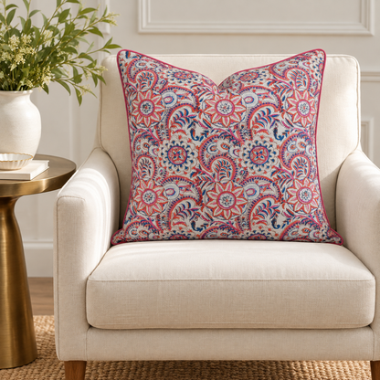 House of Mulmul - Blockprinted Cushion Covers-Pillow Cases. A square decorative throw pillow with a vibrant red, blue, and white floral paisley pattern, styled on a cream-colored armchair next to a gold side table with a white vase of greenery.