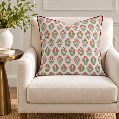 House of Mulmul - Blockprinted Cushion Covers-Pillow Cases. A square throw pillow with a red and green floral damask pattern on a white background, styled on a cream-colored armchair next to a gold side table with a white vase of greenery.