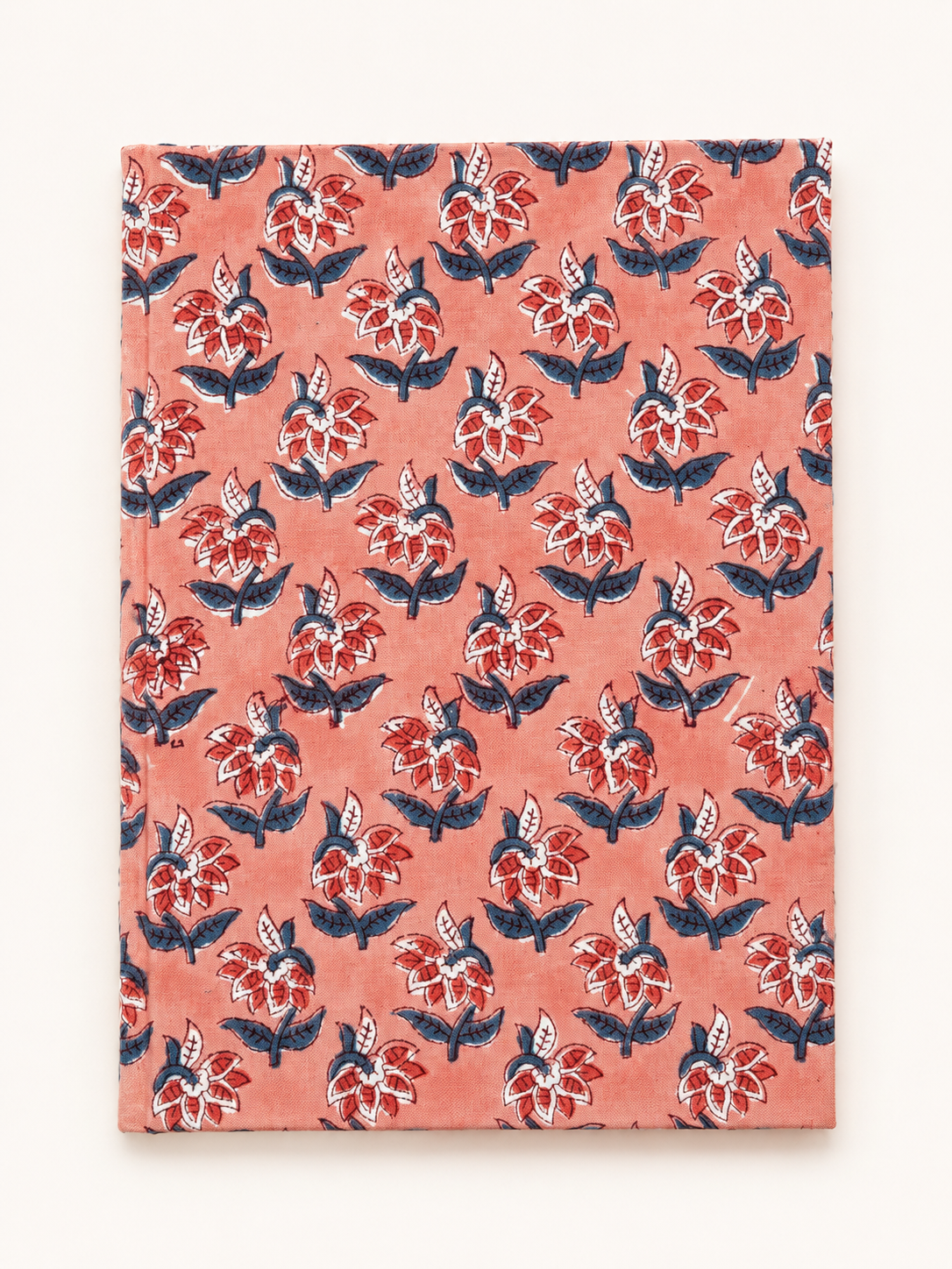 House of Mulmul - Blockprinted Journal Diary Notebook. A hardcover notebook with a coral pink cover featuring a repeating hand-painted style floral block print in red, navy blue, and white, shown against a plain off-white background.
