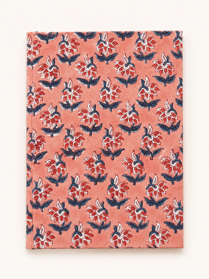 House of Mulmul - Blockprinted Journal Diary Notebook. A hardcover notebook with a coral pink cover featuring a repeating hand-painted style floral block print in red, navy blue, and white, shown against a plain off-white background.