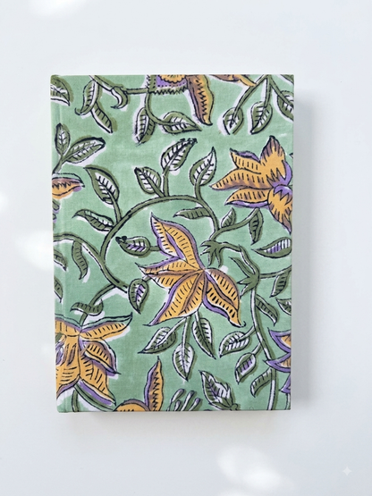 House of Mulmul - Blockprinted Journal Diary Notebook. A rectangular notebook or journal with a sage green cover featuring a hand-painted block print of yellow flowers and green leaves, displayed on a clean white background.