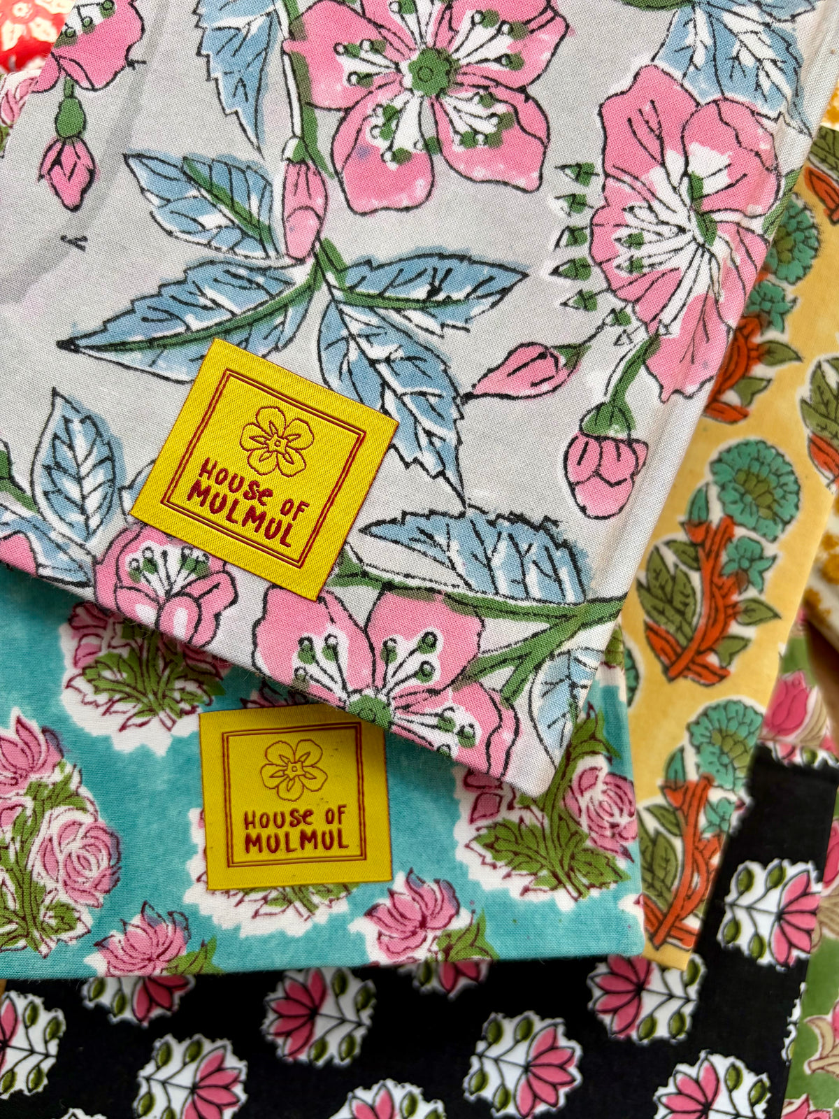 House of Mulmul - Blockprinted Journal Diary Notebook. A close-up of notebooks with pink floral prints, blue leaves, and yellow "House of Mulmul" labels on a light gray background.