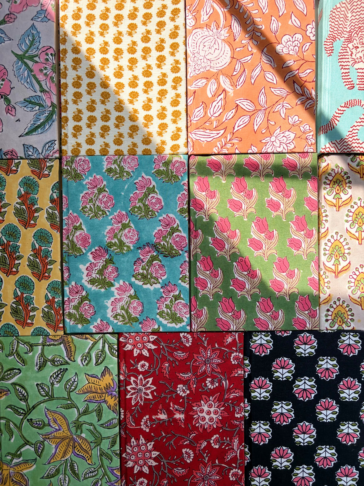 House of Mulmul - Blockprinted Journal Diary Notebook. A grid of colorful patterned notebooks arranged in a 3x4 layout, featuring various floral and geometric block prints in pink, yellow, green, red, and black.