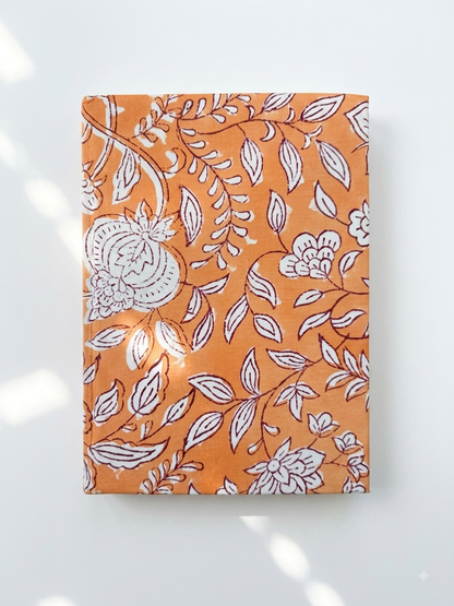 House of Mulmul - Blockprinted Journal Diary Notebook. An orange notebook with a white floral and leaf pattern, photographed flat against a light gray background with soft shadows.