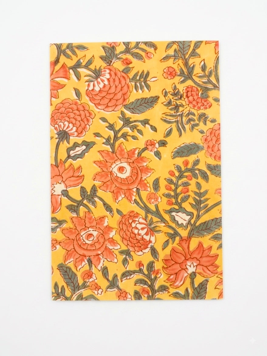 House of Mulmul - Blockprinted Journal Diary Notebook. A rectangular notebook a vibrant floral print on a bright yellow background, with orange flowers, green leaves, and small orange accents, displayed flat against a clean white background.