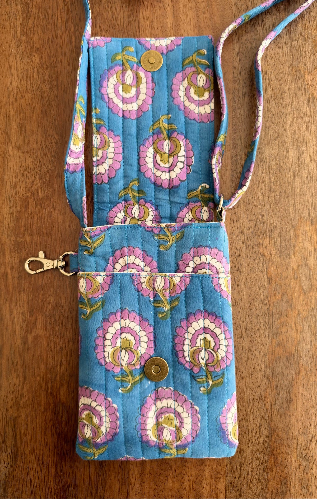 House of Mulmul - Blockprinted Mobile Sling Bag. A quilted fabric crossbody phone bag with a blue background and pink, white, and gold floral pattern, shown on a wooden surface.