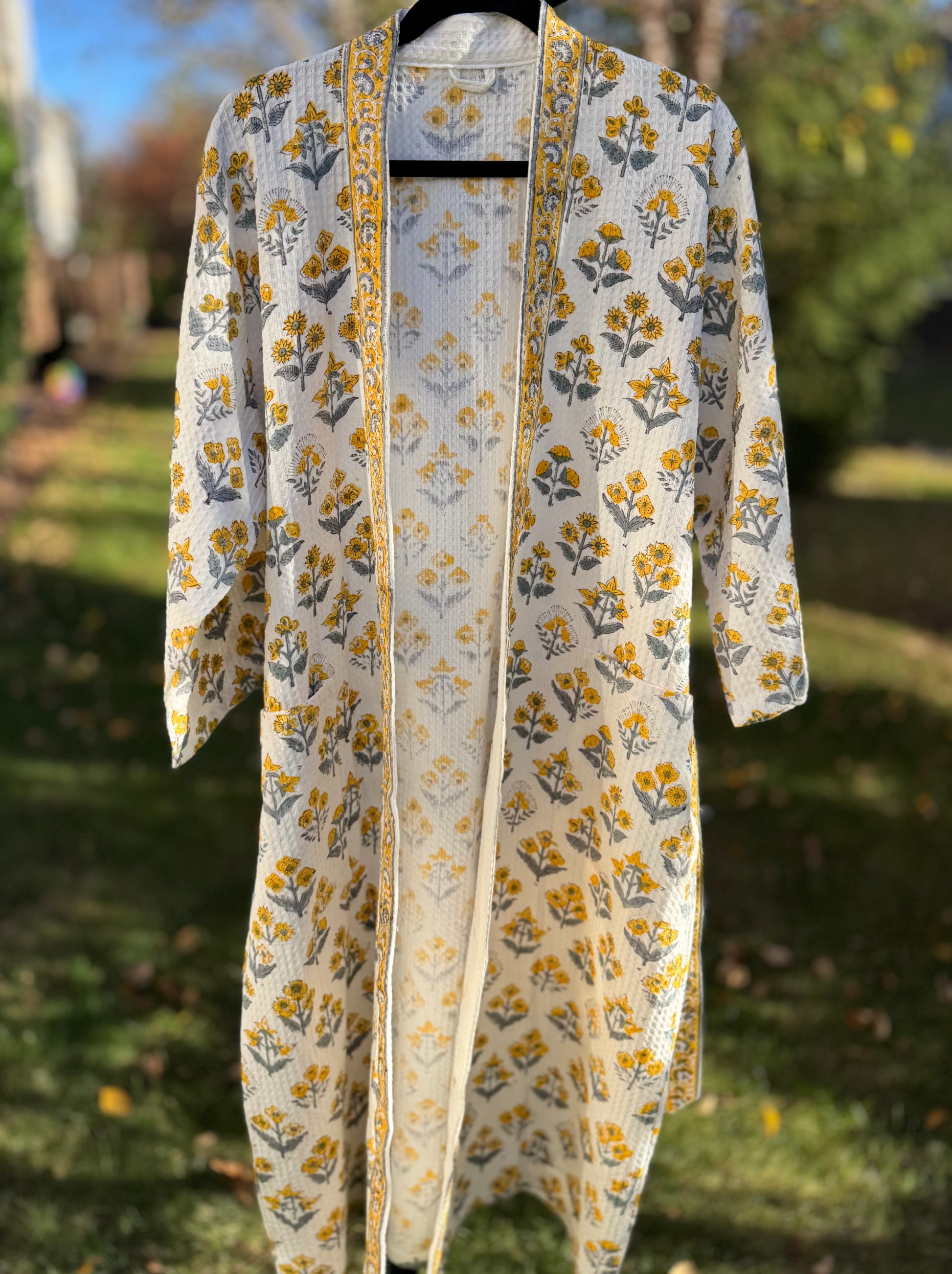 House of Mulmul - Cotton Bath robe. Floral-patterned robe  on a hanger with a blurred outdoor background