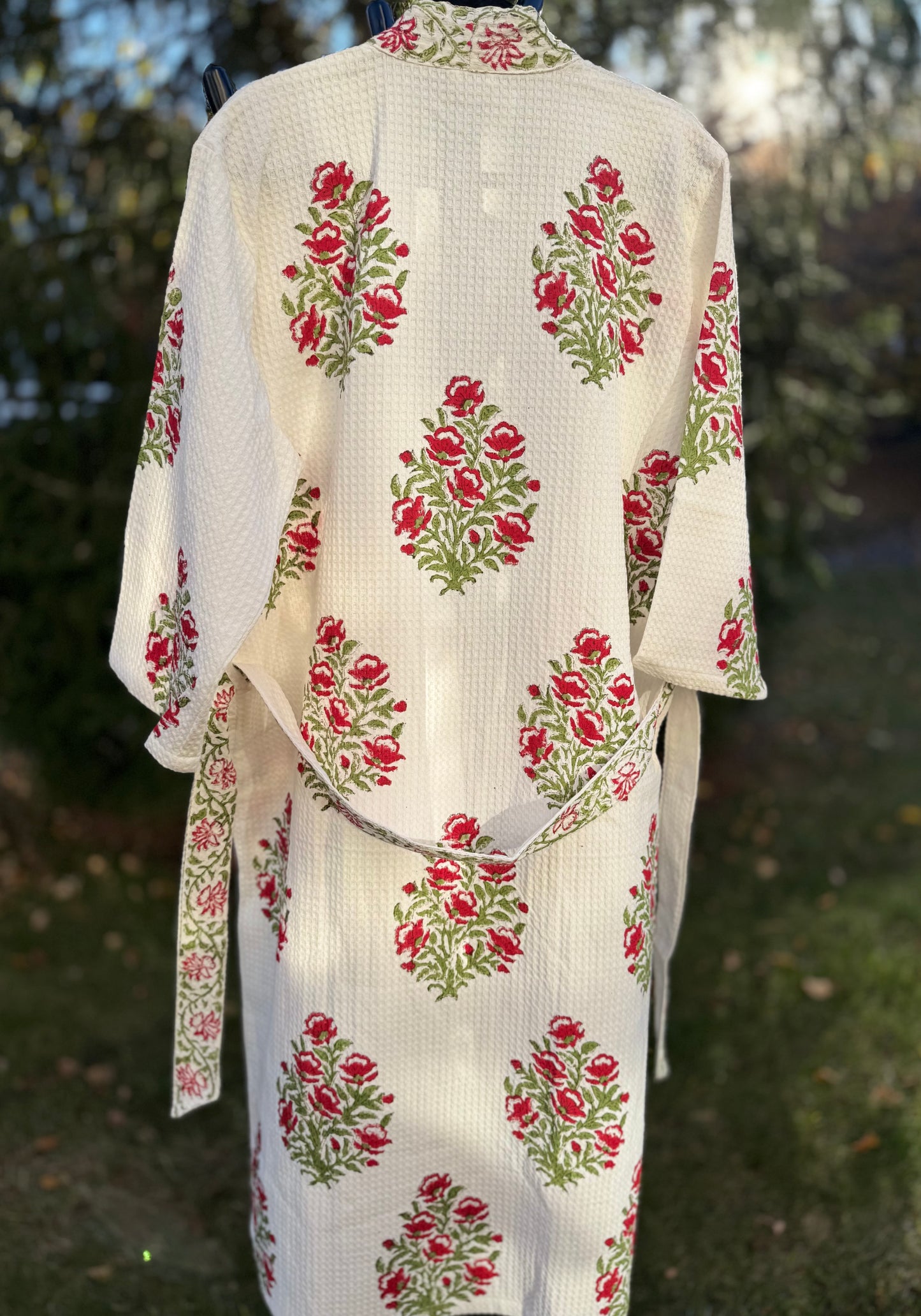 House of Mulmul - Cotton Bath robe. White bathrobe with red and green floral patterns on a blurred natural background