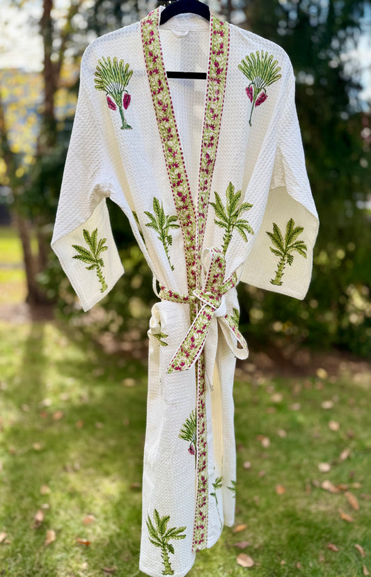 House of Mulmul - Cotton Bath robe. White embroidered robe with green and red patterns on a hanger outdoors.
