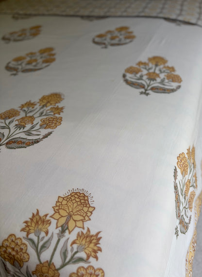 House of Mulmul - Handblock printed cotton summer quilt. Cotton coverlet. Cotton dohar. Muslin blanket. Indian summer quilt. Indian dohar. A close-up of a white fabric, likely a bedsheet or tablecloth, featuring a traditional block print pattern of mustard yellow and olive green floral motifs.