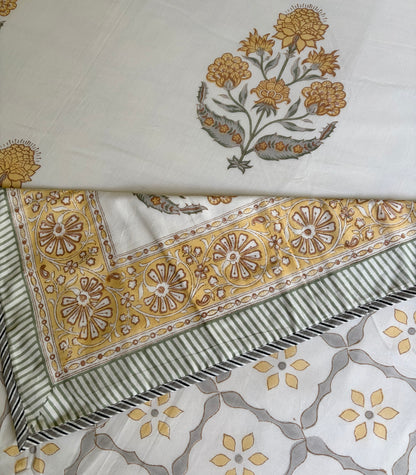 House of Mulmul - Handblock printed cotton summer quilt. Cotton coverlet. Cotton dohar. Muslin blanket. Indian summer quilt. Indian dohar. A folded and layered view of a printed fabric, showing a cream-colored base with mustard yellow and gray floral motifs, a wide decorative border with matching floral patterns, and a striped section with gray and black stripes.