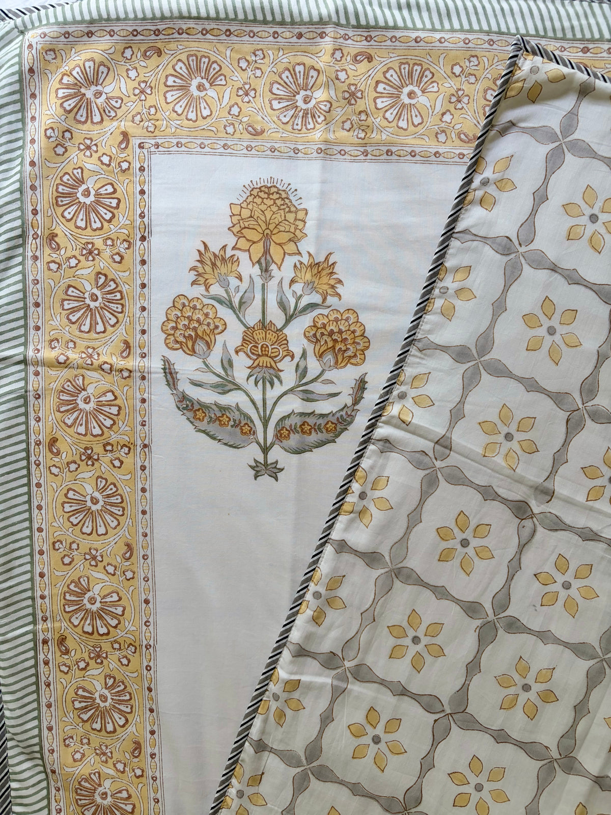 House of Mulmul - Handblock printed cotton summer quilt. Cotton coverlet. Cotton dohar. Muslin blanket. Indian summer quilt. Indian dohar. A folded patterned textile, likely a scarf or shawl, showing a cream base with a yellow and brown floral motif on one side and a repeating yellow and brown geometric lattice pattern on the other, bordered by a striped edge.