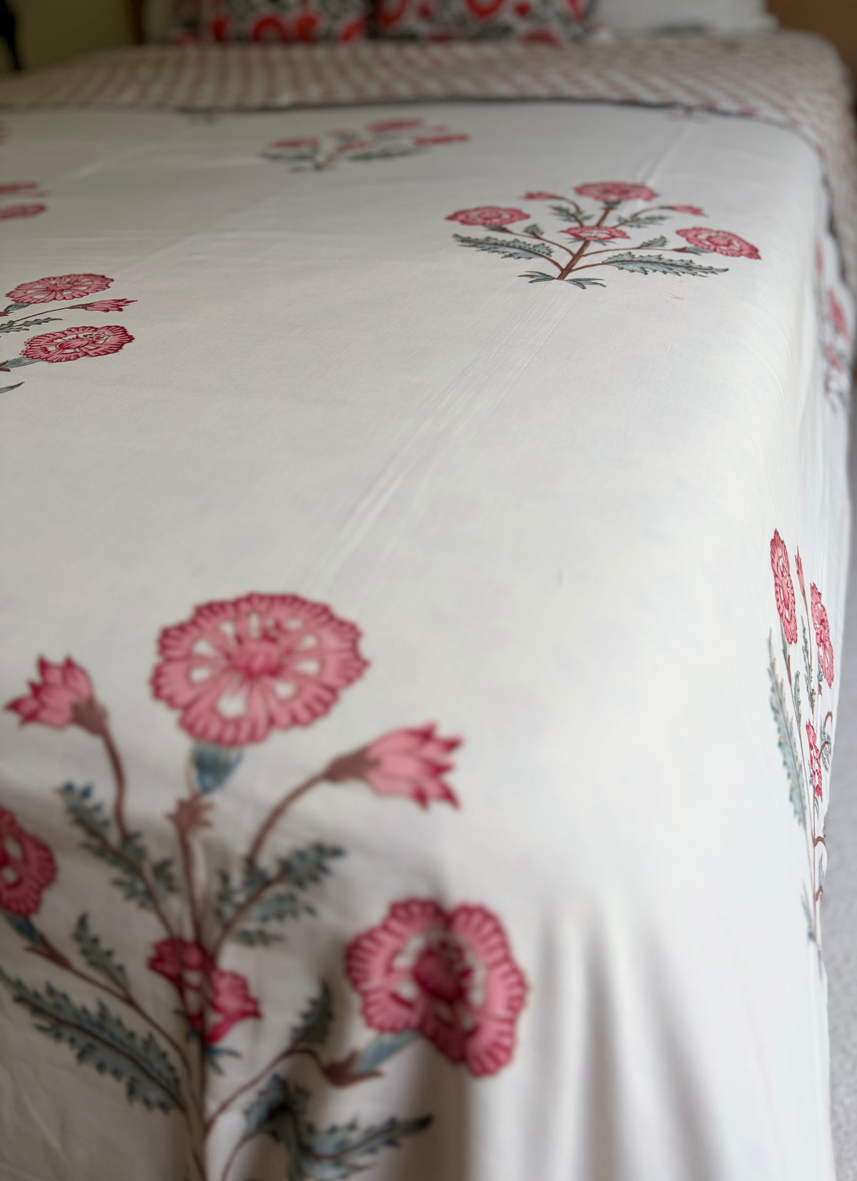 House of Mulmul - Handblock printed cotton summer quilt. Cotton coverlet. Cotton dohar. Muslin blanket. Indian summer quilt. Indian dohar. A close-up of a white or off-white bedding surface, likely a duvet cover or comforter, printed with pink flowers and muted green-gray leaves in a repeating floral pattern.