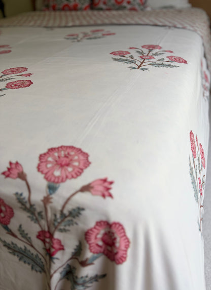 House of Mulmul - Handblock printed cotton summer quilt. Cotton coverlet. Cotton dohar. Muslin blanket. Indian summer quilt. Indian dohar. A close-up of a white or off-white bedding surface, likely a duvet cover or comforter, printed with pink flowers and muted green-gray leaves in a repeating floral pattern.
