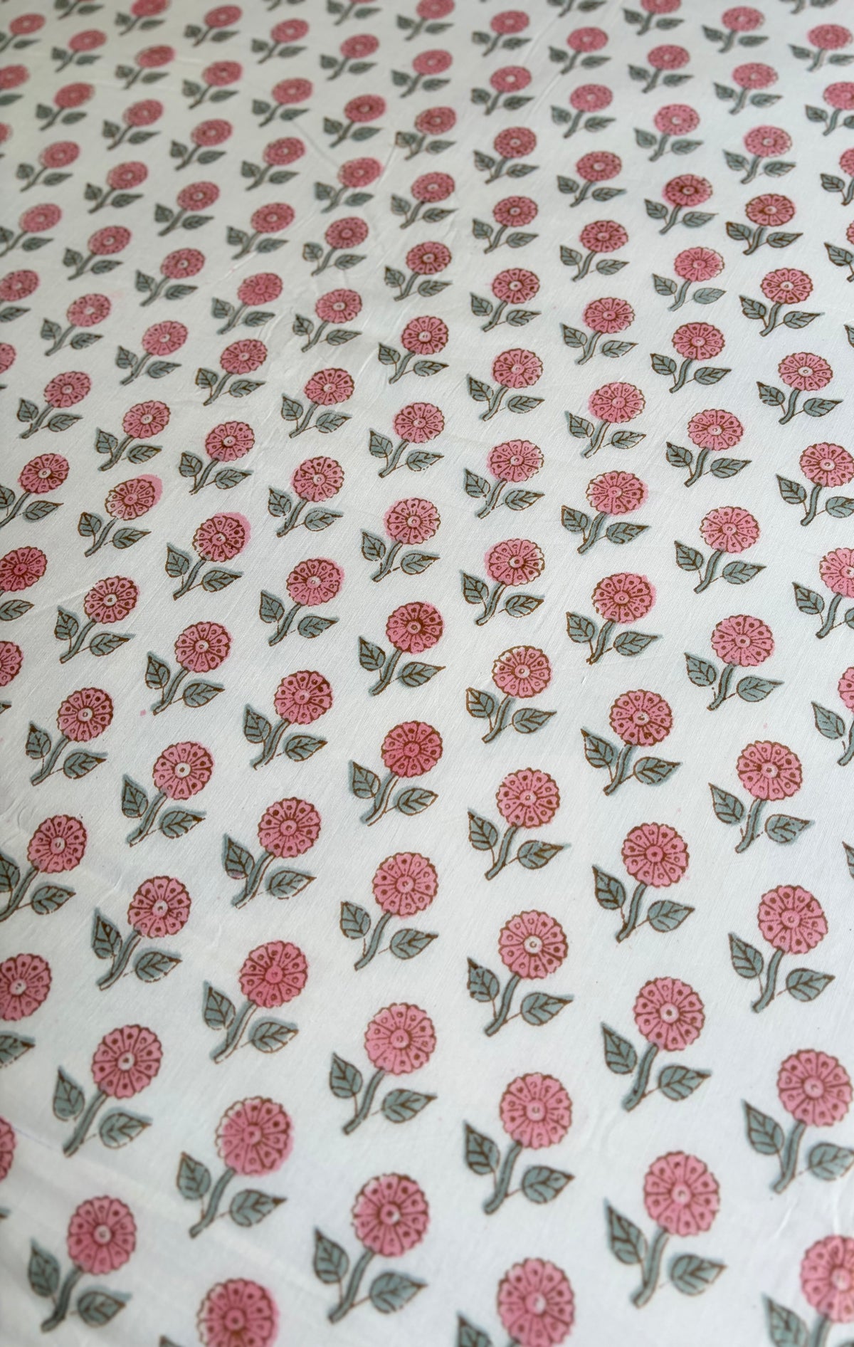 House of Mulmul - Handblock printed cotton summer quilt. Cotton coverlet. Cotton dohar. Muslin blanket. Indian summer quilt. Indian dohar. A close-up of a white fabric with a repeating block-print style floral pattern in dusty pink and muted green.