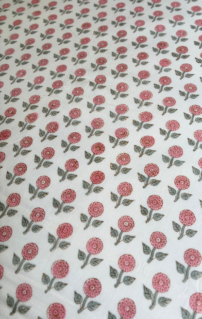 House of Mulmul - Handblock printed cotton summer quilt. Cotton coverlet. Cotton dohar. Muslin blanket. Indian summer quilt. Indian dohar. A close-up of a white fabric with a repeating block-print style floral pattern in dusty pink and muted green.
