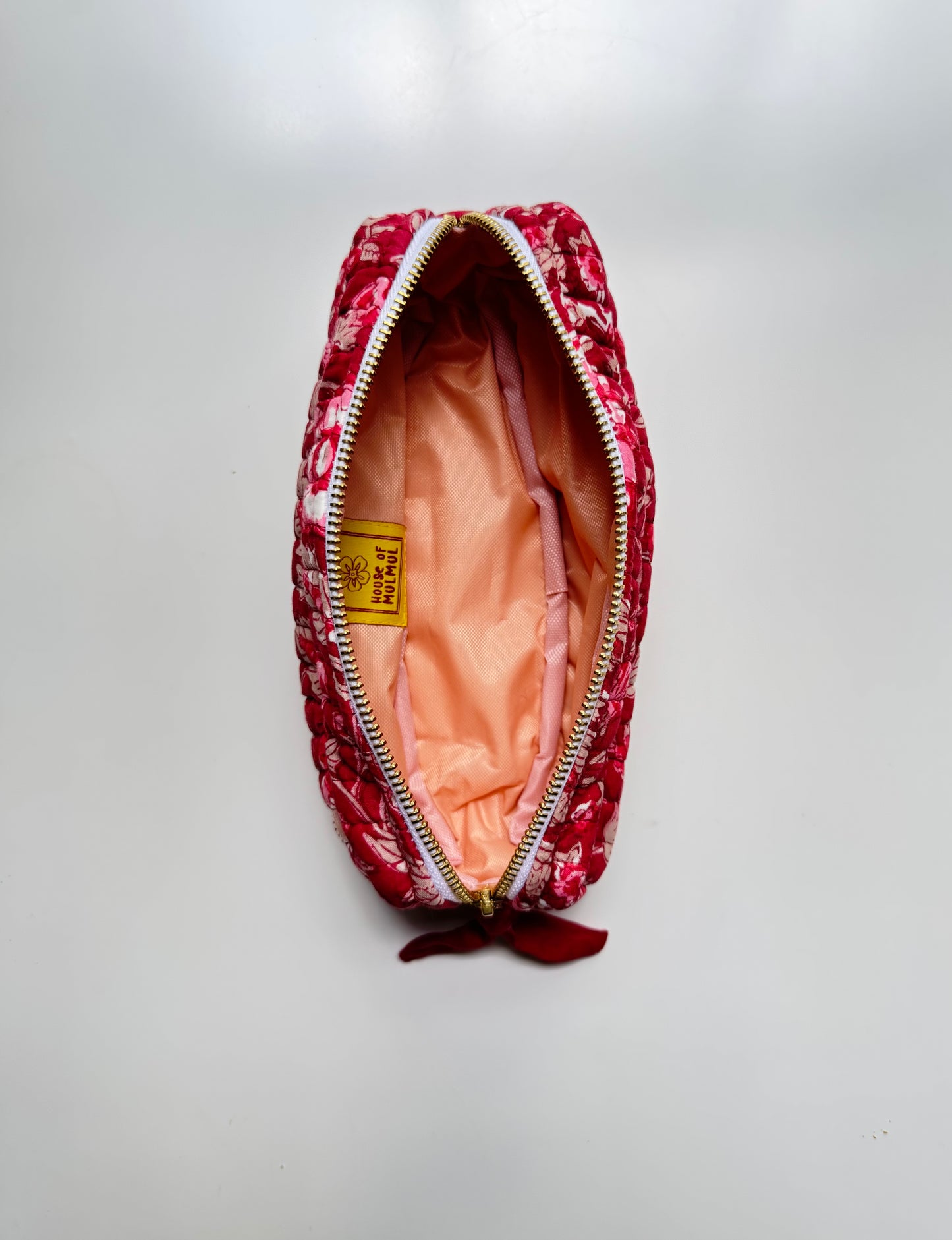 House of Mulmul - Cotton Quilted Makeup Barrel Pouch. A red and white floral patterned zippered pouch with a peach-colored interior lining and a small red ribbon bow at the bottom, shown open on a light gray background.