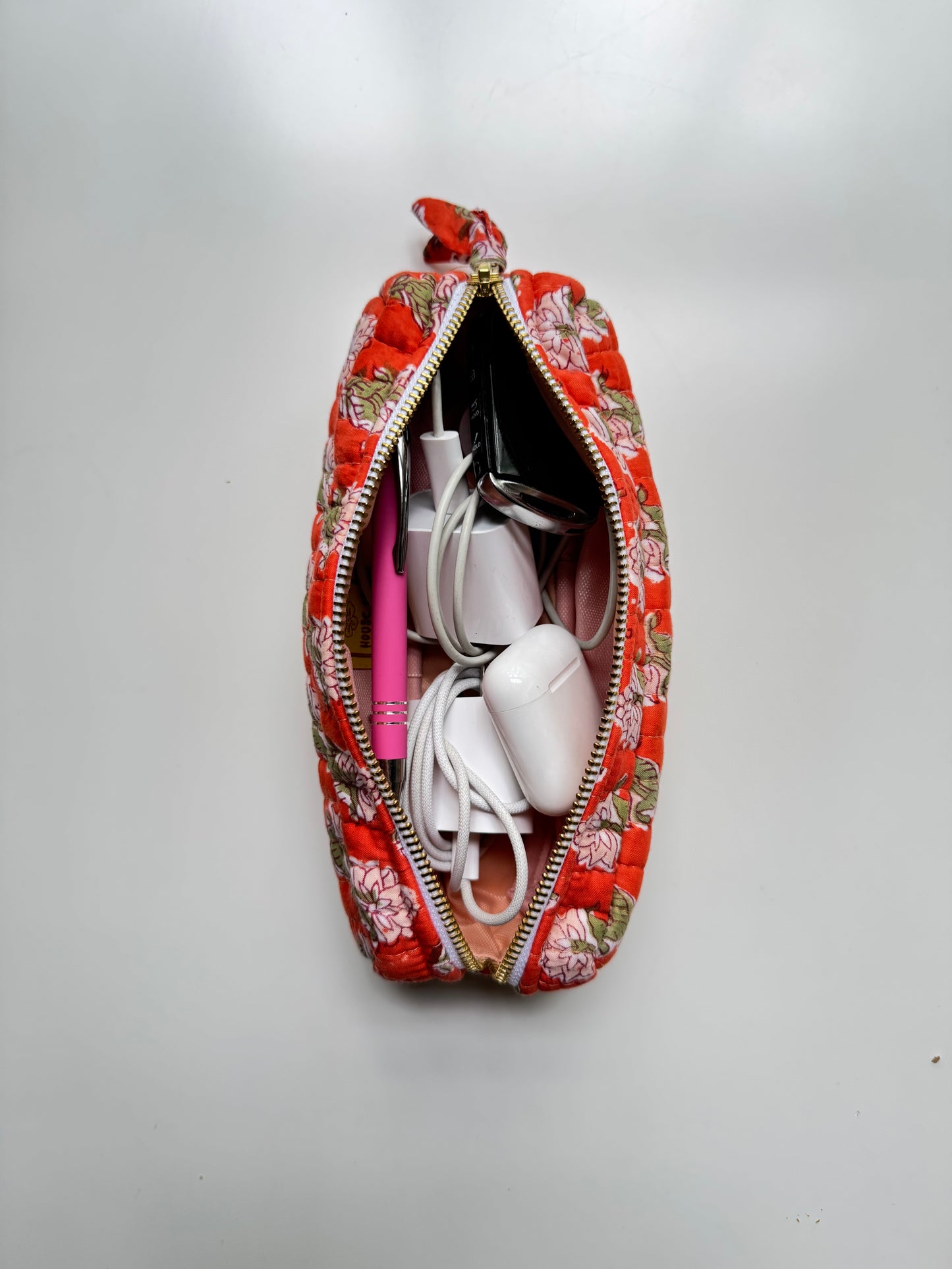 House of Mulmul - Cotton Quilted Makeup Barrel Pouch. A red floral zippered pouch shown open from a top-down view, filled with white cables and a pink item, on a plain light gray background.