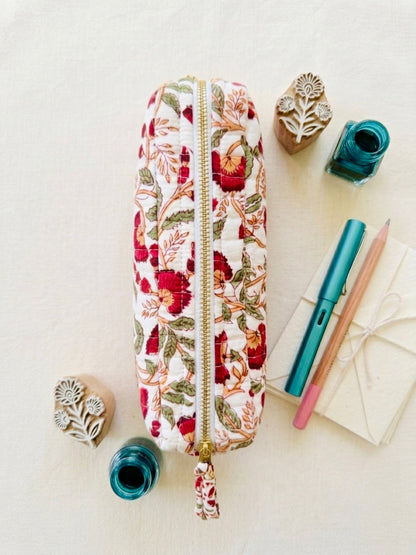 House of Mulmul - Cotton Quilted Makeup Barrel Pouch. A fabric zippered pencil case with a red and green floral print, styled in a flat lay with stationery and rubber stamps on a light cream background.