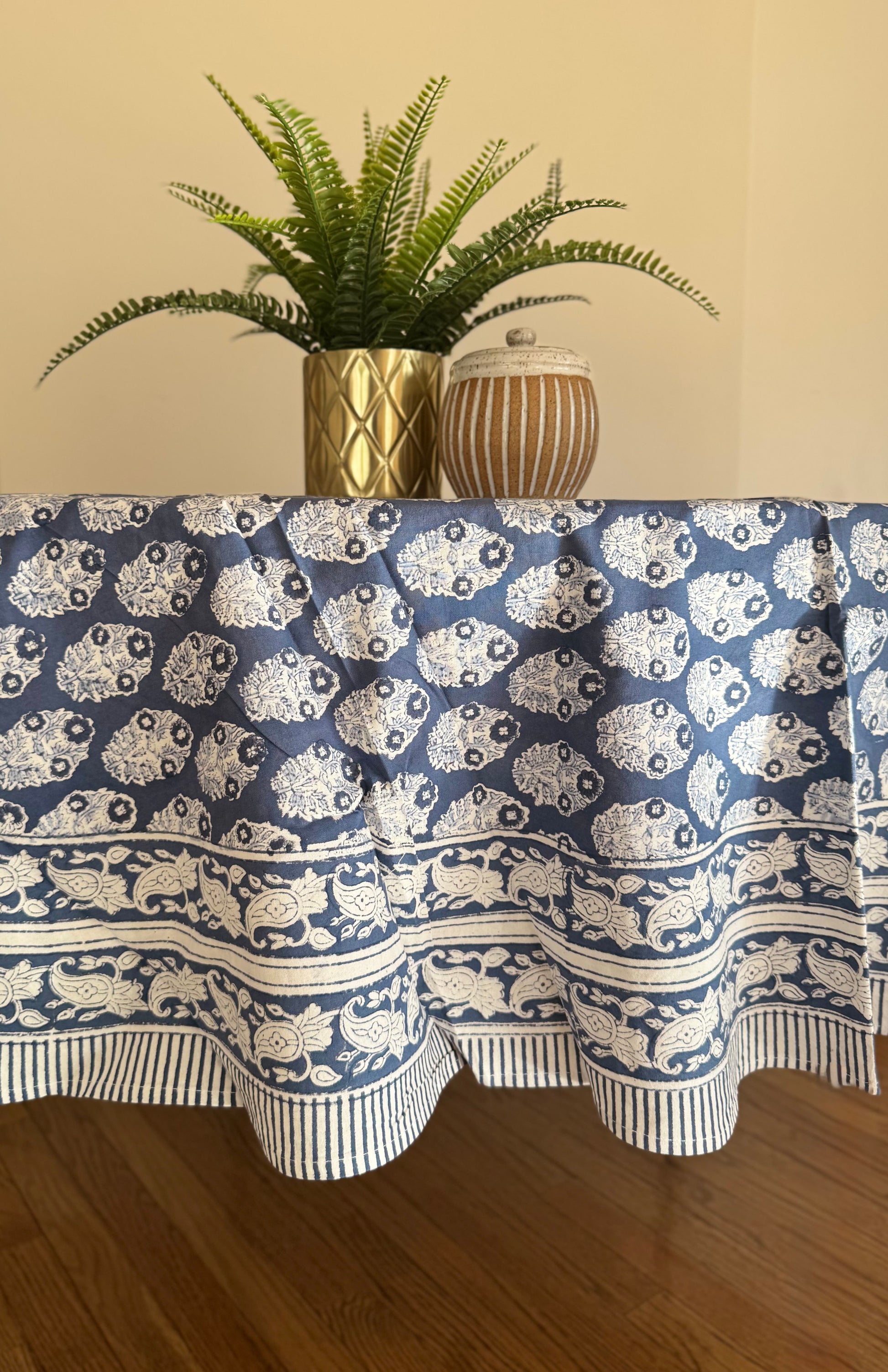 House of Mulmul - Cotton Table Cloth Round. Tablecloth with blue and white pattern on a wooden table with plants in the background