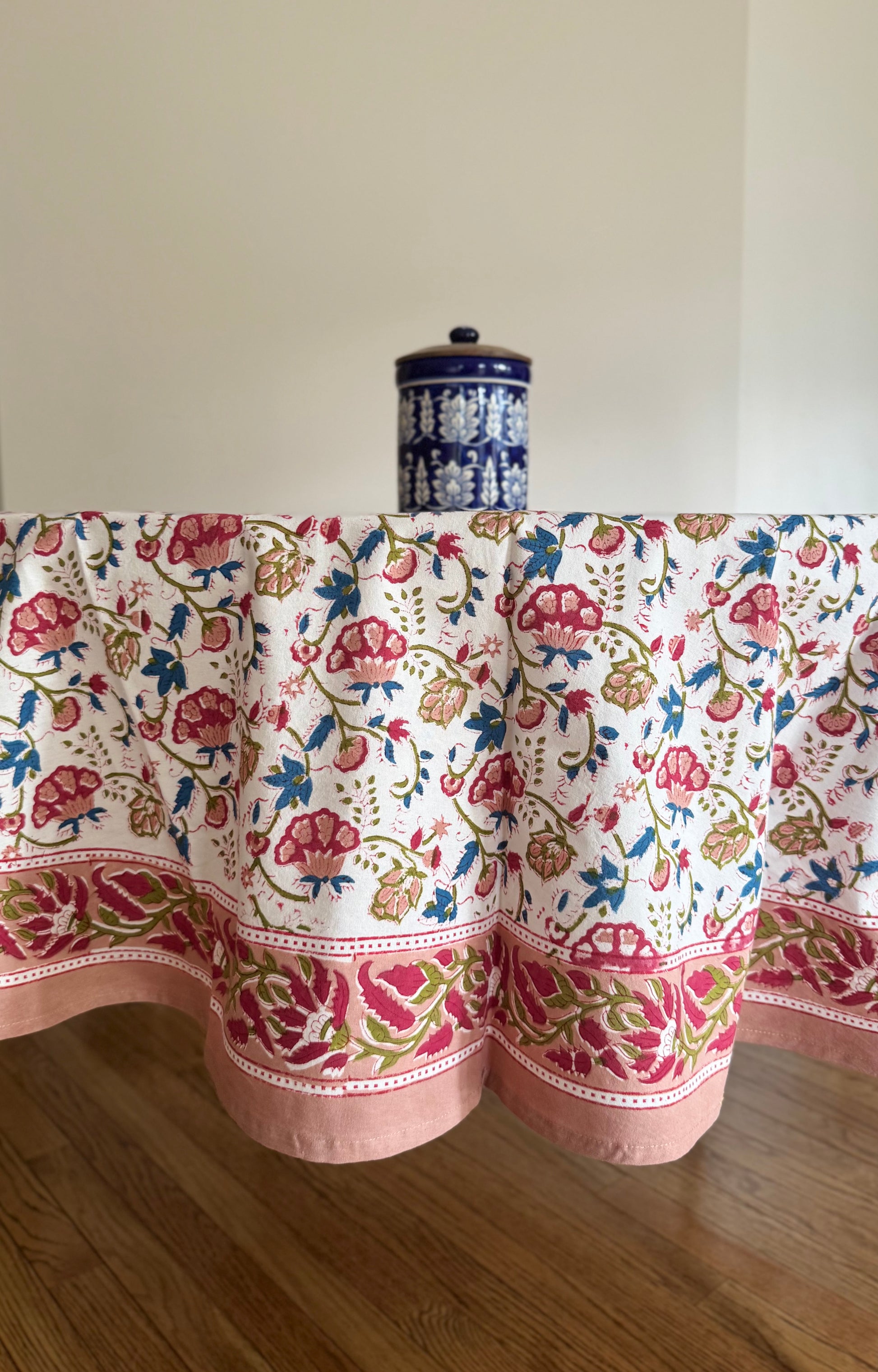 House of Mulmul - Cotton Table Cloth Round. Floral patterned tablecloth on a wooden table with a white wall background