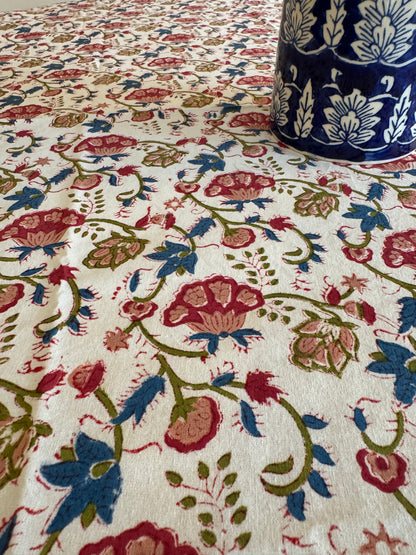 House of Mulmul - Cotton Table Cloth Round. Close-up of floral patterned fabric with a blue pillow partially visible.
